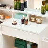 A close-up view of a white vanity table with various skincare products arranged on its surface and shelves. Voir les images du produit