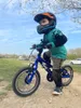 A young child wearing a helmet and protective gear rides a blue bicycle on a dirt path. Náhľad obrázku produktu