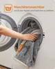 A hand is placing a gray blanket into a washing machine. Produktbild-Vorschau
