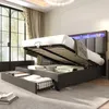A bedroom scene with a bed that has storage compartments open, revealing luggage and folded linens. The bed has an upholstered headboard with LED lighting. Produktbild-Vorschau