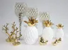 A collection of decorative items including pineapples, candle holders, and bird figurines, arranged on a white surface. Anteprima dell’immagine prodotto