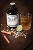 A bottle of Remedy Spiced Rum, a glass of rum with ice and lemon, and various spices are arranged on a wooden surface. Náhled obrázku produktu
