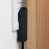 A close-up shot of a black power strip plugged into a white wall socket, with a wooden surface to the right. Produktbild-Vorschau
