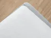 A close-up of a white mattress protector with a gray edge, placed on a wooden floor. Produktbild-Vorschau