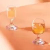 Two wine glasses filled with a light yellow liquid are placed on a peach-colored surface with soft shadows. Podgląd zdjęcia produktu