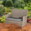 A polyrattan bench with a gray cushion is placed on a wooden deck in a garden setting with flowers and greenery. Produktbild-Vorschau