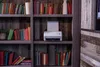 A white printer sits on a bookshelf filled with books. Voir les images du produit