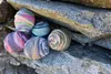 Several balls of colorful yarn are arranged on a rocky surface. Produktbild-Vorschau