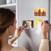 A woman is placing a photo frame on a refrigerator door. Produktbild-Vorschau