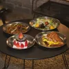 Four plates of food are arranged on a dark round table, with a blurred background suggesting an outdoor or rustic setting. Náhled obrázku produktu