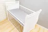 A white baby crib with a grey and white star-patterned fitted sheet. Produktbild-Vorschau