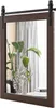 A dark brown wooden framed mirror with a barn door sliding mechanism is shown hanging on a wall. A large green plant in a vase is reflected in the mirror, along with sheer curtains and a stack of books on a table. Podgląd zdjęcia produktu