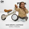 A young child sits next to a balance bike, smiling. Voir les images du produit