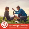 Two people are outdoors in a grassy area, with one person applying a tourniquet to the other's leg. Produktbild-Vorschau
