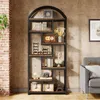 A tall, arched bookshelf filled with decorative items and books, placed in a room with a brick wall and a sofa. Náhled obrázku produktu