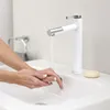 A person washing their hands under a modern white and silver faucet in a bathroom sink. Produktbild-Vorschau