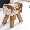 A close-up studio shot of a turnbock-style stool with a cowhide-like pattern and wooden legs. Produktbild-Vorschau