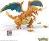 A LEGO-style buildable toy Charizard Pokémon figure with its wings spread, breathing fire. Small accessory pieces and a Poké Ball are scattered around it on a white background. Voir les images du produit