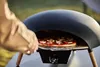 A person is using a pizza oven outdoors to cook a pizza. Produktbild-Vorschau