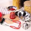 A collection of canning tools, including a jar lifter and funnels, are arranged on a countertop with jars of pasta and spaghetti in the background. Produktbild-Vorschau