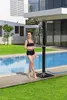 A woman is standing next to a swimming pool, using an outdoor shower. Produktbild-Vorschau