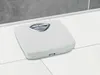 A white analog bathroom scale is placed on a tiled floor, with a gray tiled wall in the background. Produktbild-Vorschau