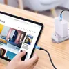 A hand is holding a tablet that is charging via a USB-C cable connected to a power adapter plugged into a wall socket. Anteprima dell’immagine prodotto