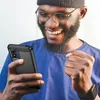 A man is happily looking at his phone while holding it in his hand. Produktbild-Vorschau