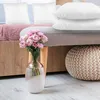 A bedroom scene with pillows, a vase of flowers, and a pouf. Produktbild-Vorschau