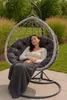A woman is relaxing in a hanging egg chair outdoors, covered with a blanket. Produktbild-Vorschau