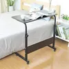 A mobile C-shaped side table with a dark brown top and black metal frame is placed next to a bed. The table has a book and a cup on it, and a small shelf with books is attached to the side. The scene is set in a bedroom. Anteprima dell’immagine prodotto