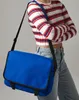A person wearing a striped shirt and jeans, carrying a blue messenger bag. Anteprima dell’immagine prodotto