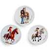 Three round images, each featuring a cartoon girl with a horse. The top image shows a girl standing next to a horse. The bottom left image shows a girl riding a brown horse. The bottom right image shows a girl riding a white horse. Produktbild-Vorschau