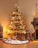 A Christmas tree decorated with lights and ornaments, surrounded by gifts and a rug, with a fireplace and stocking in the background. Podgląd zdjęcia produktu