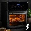 A black air fryer with food inside, placed on a dark surface with a plant in the background. Produktbild-Vorschau