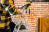 A person is using a step ladder indoors, with a brick wall in the background and part of a yellow armchair visible on the right. Anteprima dell’immagine prodotto