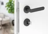 Close-up of a door handle and lock mechanism on a white door, with a blurred interior scene in the background. Produktbild-Vorschau