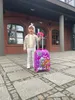 A young girl stands with a suitcase in front of a building. Anteprima dell’immagine prodotto
