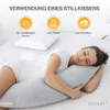 A woman is sleeping on a bed, hugging a long gray pillow. There are icons and text above her indicating the uses of the pillow. Produktbild-Vorschau