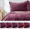 A close-up view of a quilted bedspread and pillow in a berry/mauve color, with a wicker chair and blanket in the background. Below the main image are five smaller images demonstrating the color under different lighting conditions. Produktbild-Vorschau