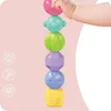 A baby's hand stacking colorful geometric shapes on a pink background. Produktbild-Vorschau