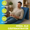 A man is reading a book while sitting on a blue foldable mattress in a living room. Produktbild-Vorschau