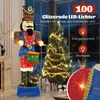 A large, illuminated nutcracker figure stands next to a decorated Christmas tree in a room with a fireplace and window. Podgląd zdjęcia produktu
