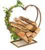 A heart-shaped metal log holder filled with firewood, decorated with artificial ivy. Produktbild-Vorschau