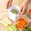 Hands are using a white vegetable slicer to cut cucumbers, with pre-cut carrots, cucumbers, and potatoes laid out on a wooden cutting board. Produktbild-Vorschau