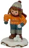 Ein kleines Mädchen in einem orangefarbenen Pullover und blauer Hose steht auf einer schneebedeckten Fläche mit Schneebällen in den Händen und trägt eine graue Mütze sowie einen roten Schal. Produktbild-Vorschau