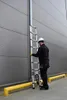 A person is using an aluminum telescopic ladder against a building wall. Náhľad obrázku produktu