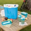A picnic setup on a wooden table with a blue cooler, food, and drinks. Podgląd zdjęcia produktu