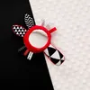 A black and white baby toy with a mirror and red accents is placed on a surface divided into black and white sections. Produktbild-Vorschau