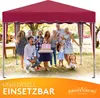 A group of people, including adults and children, are gathered under a red canopy tent in an outdoor setting, possibly a party or celebration. Some people are holding drinks and a cake is being presented. Produktbild-Vorschau